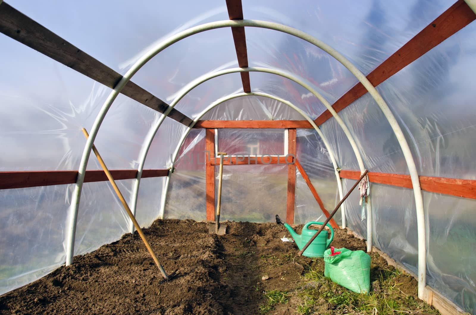 early spring time greenhouse inside construction with gardener tools and earth soil