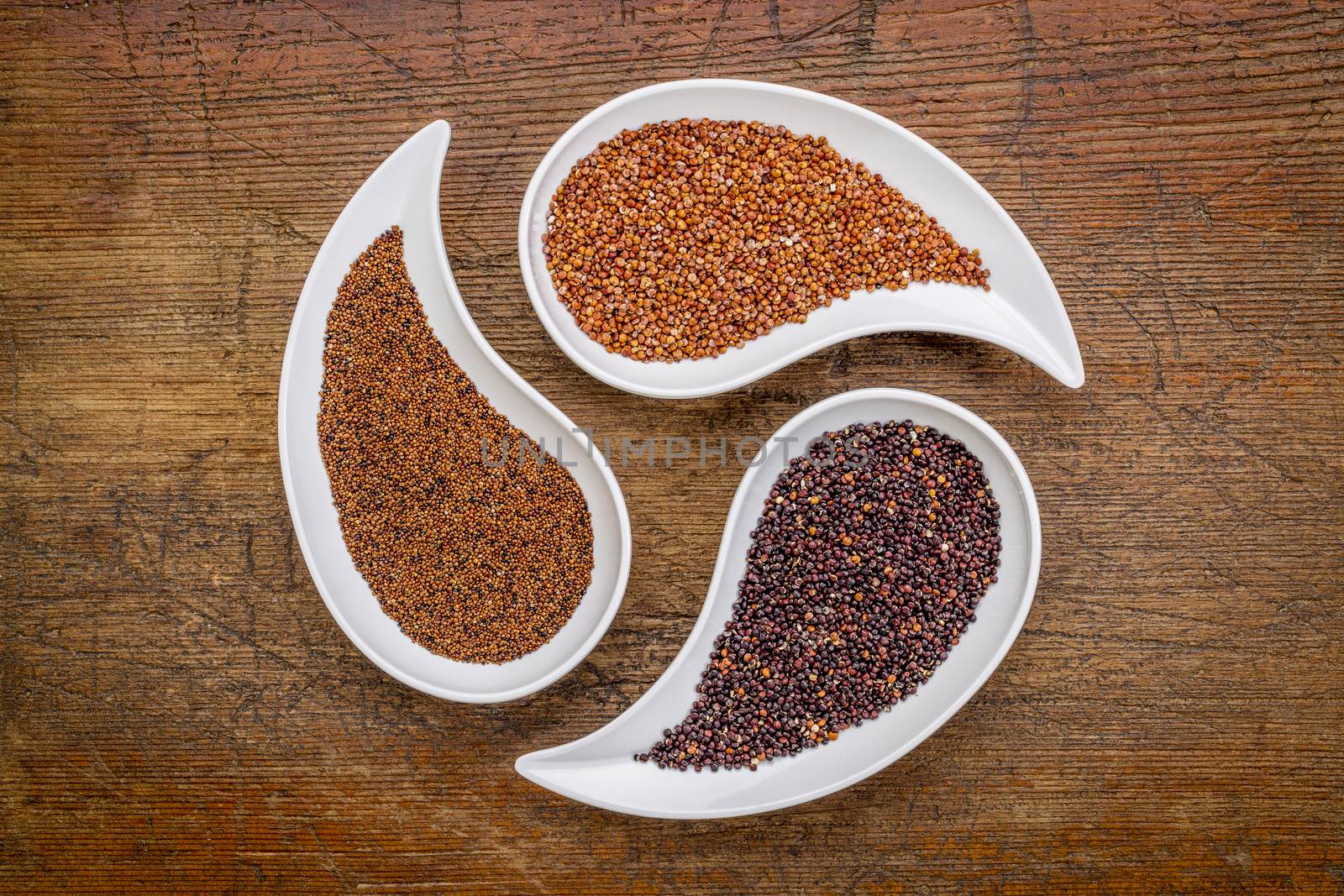 kaniwa, red and black quinoa - three gluten free grains in teardrop shaped bowls against rustic wood