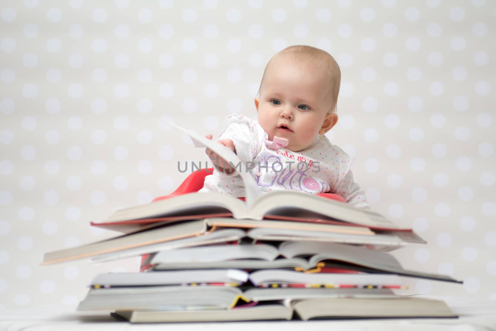 Cute baby girl sitting behind a pile of books