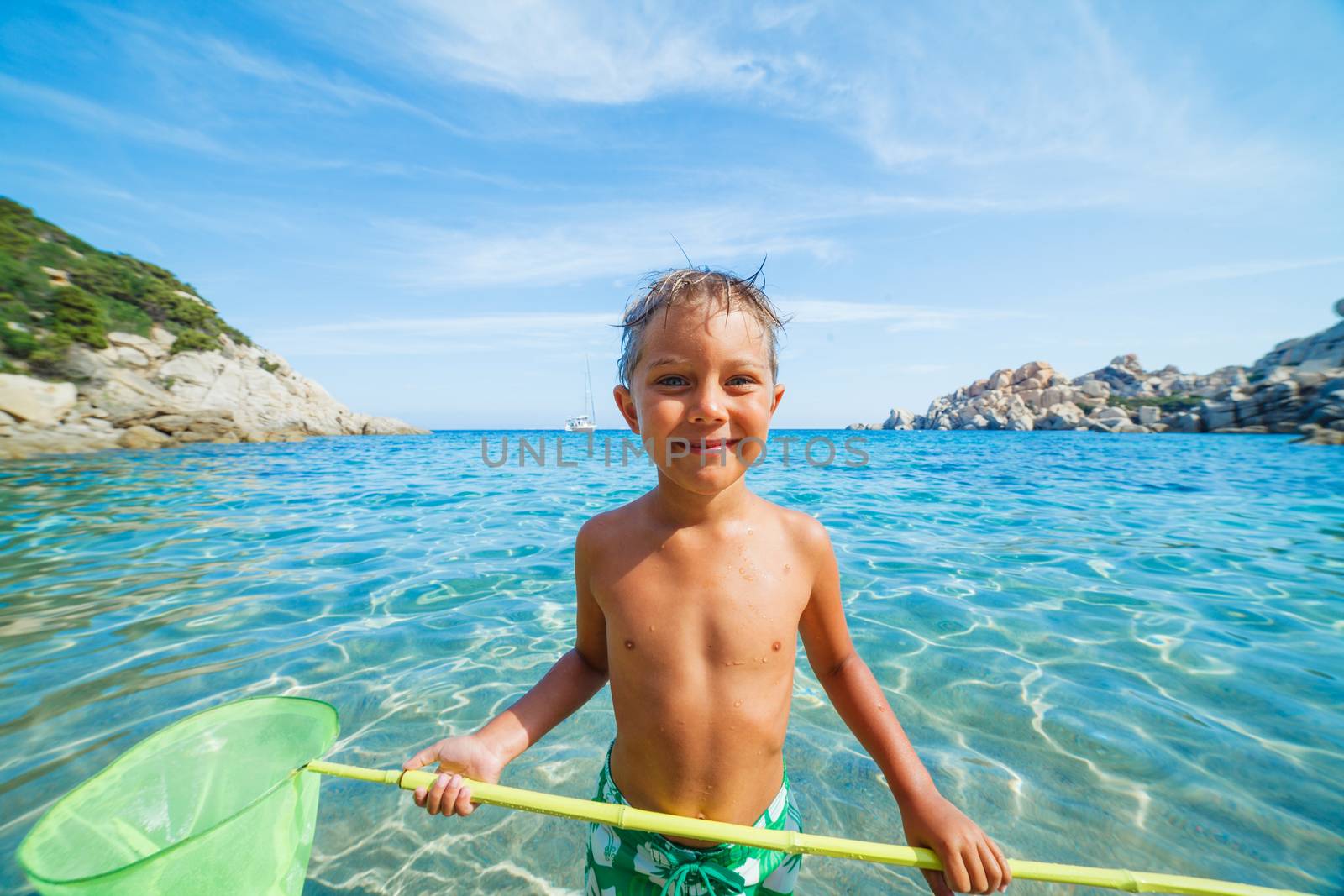 Cute boy playing with scoop-net and swimming in the transparent sea