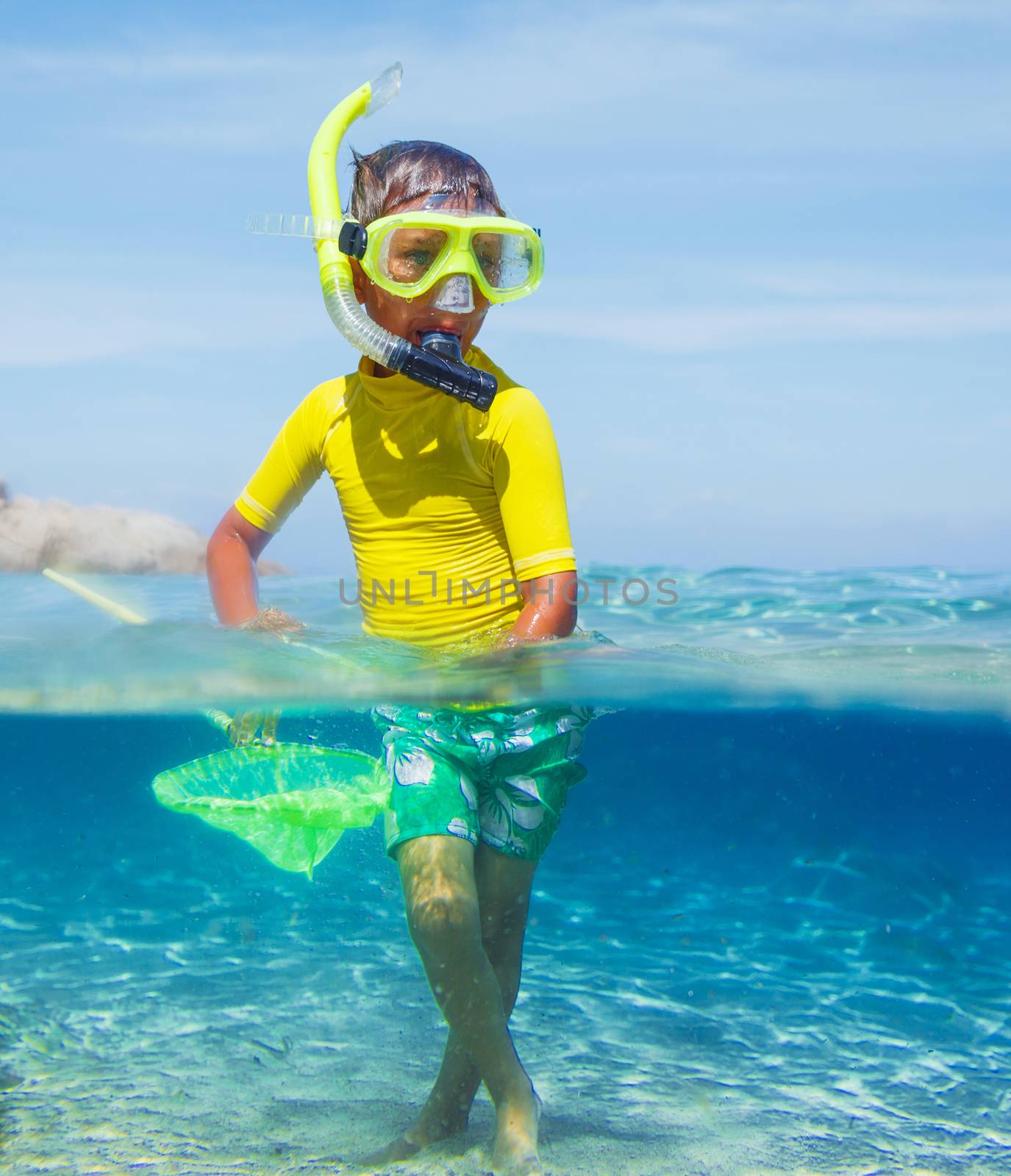 Cute boy playing with scoop-net and swimming in the transparent sea