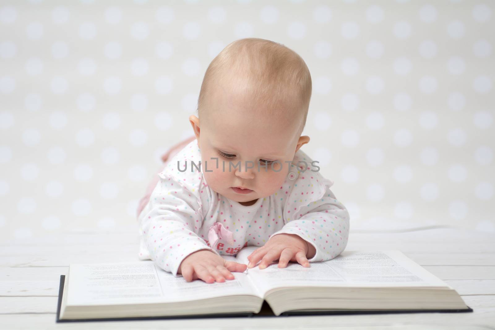 Baby girl lying on the belly reading a book