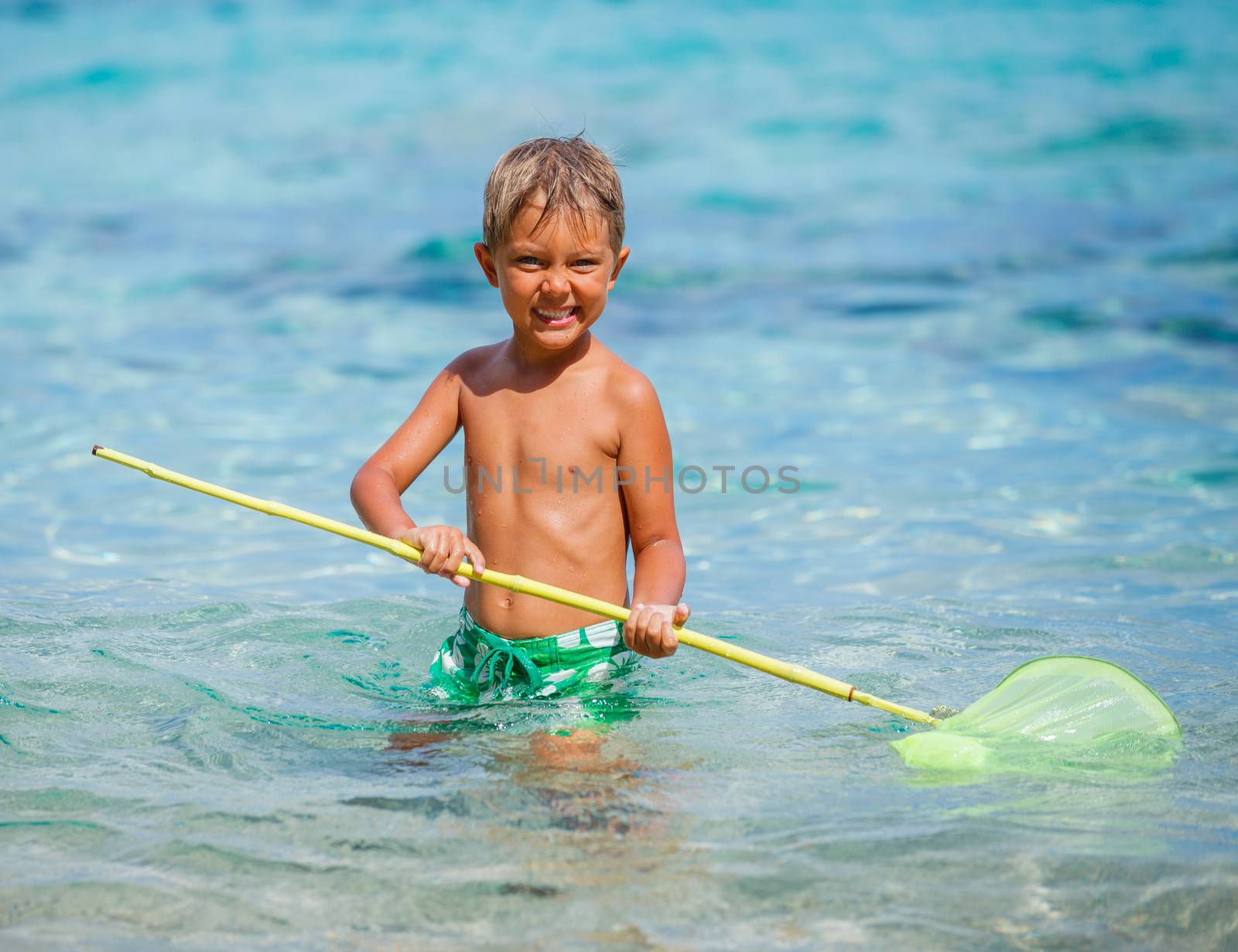 Cute boy playing with scoop-net and swimming in the transparent sea