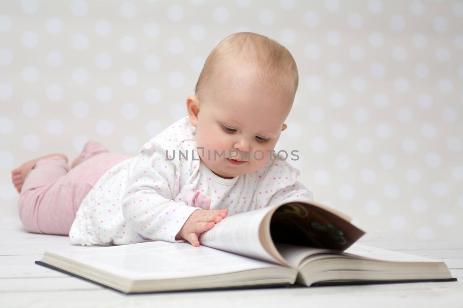 Baby girl lying on the belly reading a book