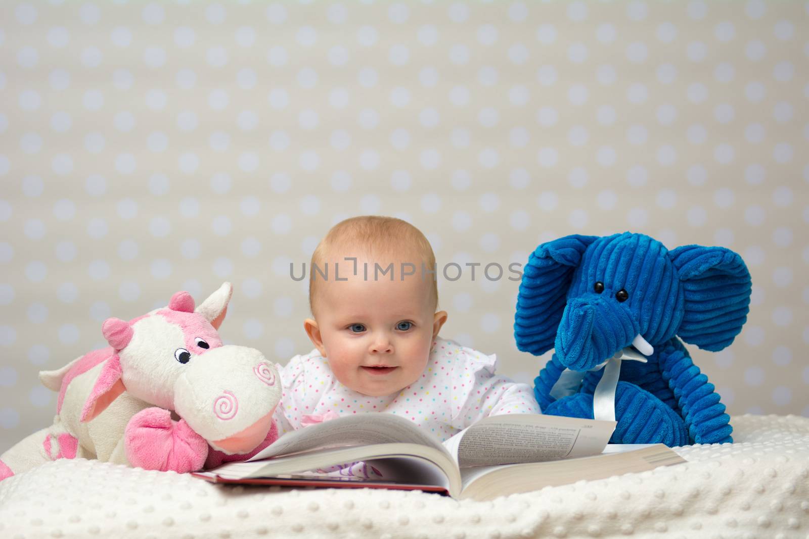 Happy baby girl reading a book with little friends