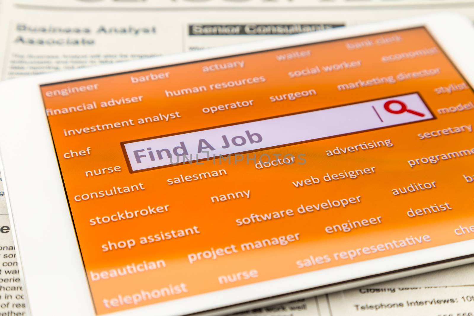 Orange tablet screen fill with difference career words.  Internet website for online job search having wording "find a job" and searching symbol in search engine box. Blur classifieds ads on background.