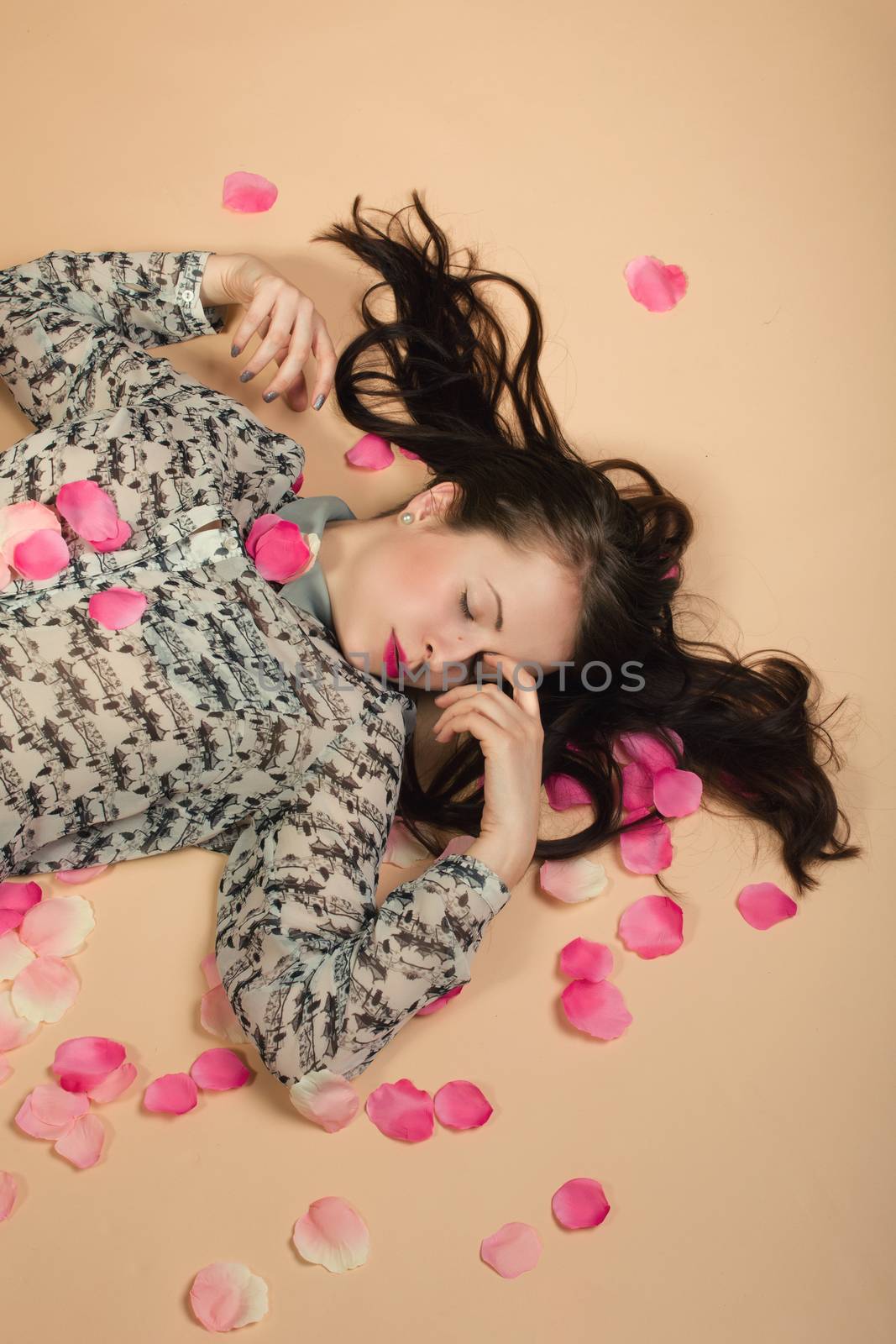 atractive brunette girl lying on beige background, dreaming and sleeping with rose petals around. Beaty concept.