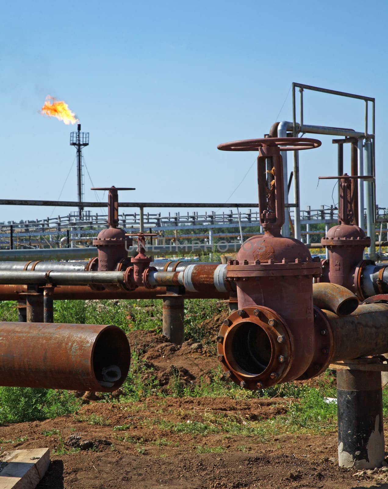 Rusty pipeline with valves on the foreground. Oil flame torch on the background