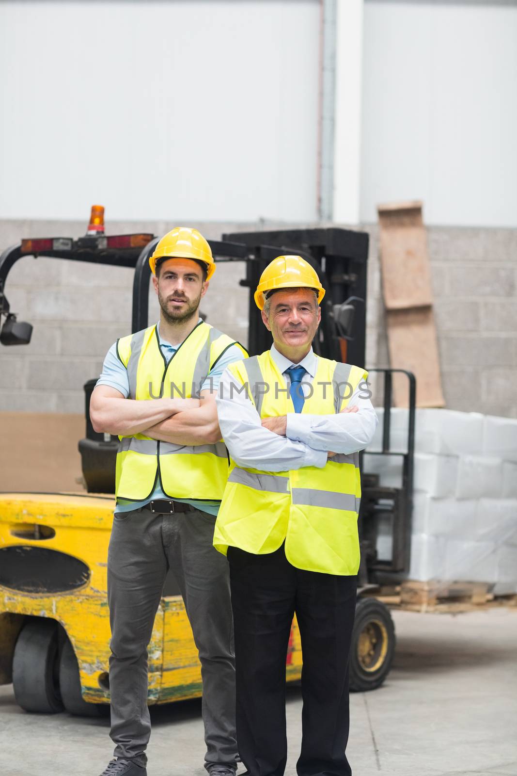Manager with arms crossed and his colleague behind him in warehouse
