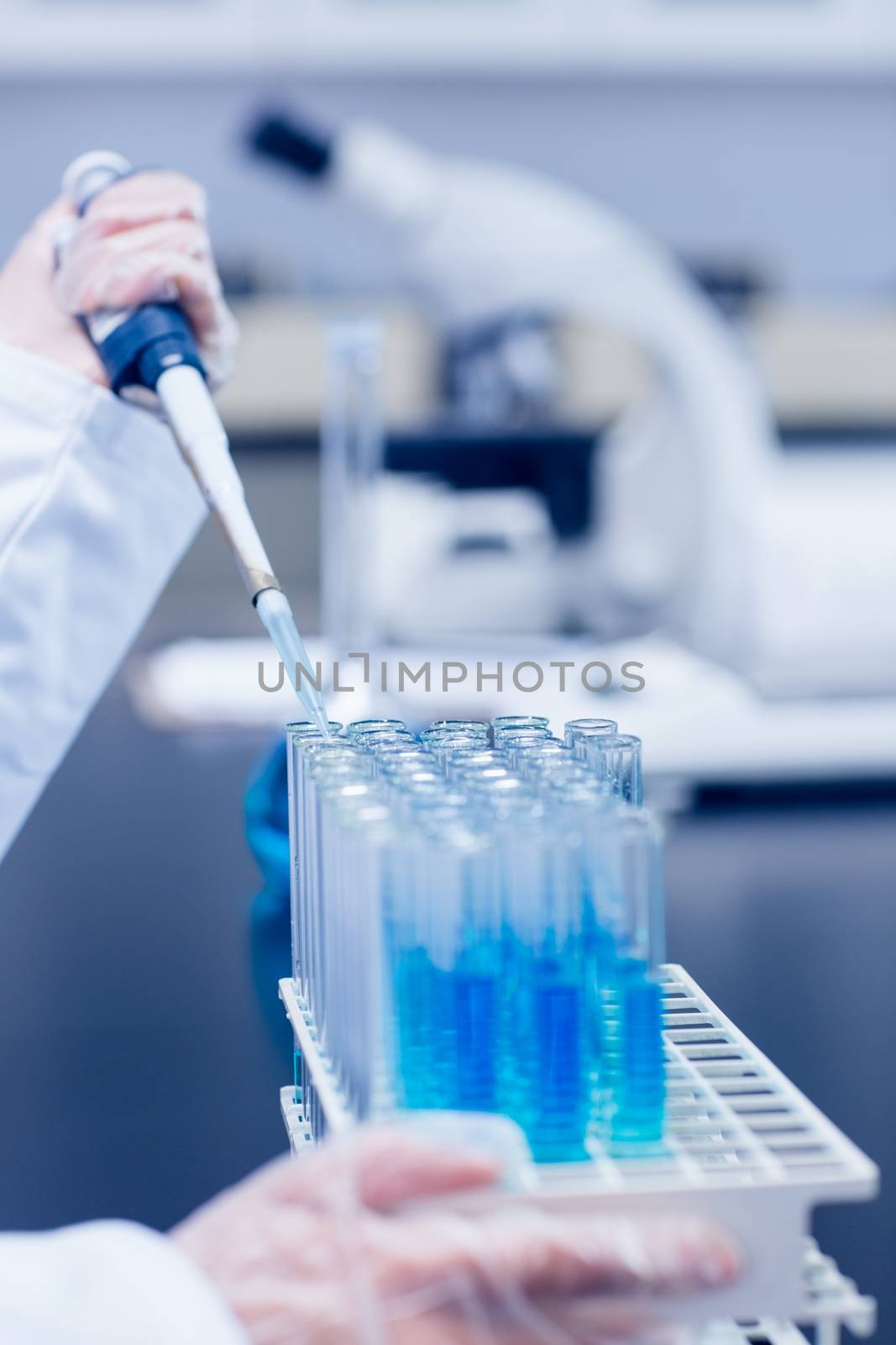 Science student using pipette in the lab to fill test tubes by Wavebreakmedia