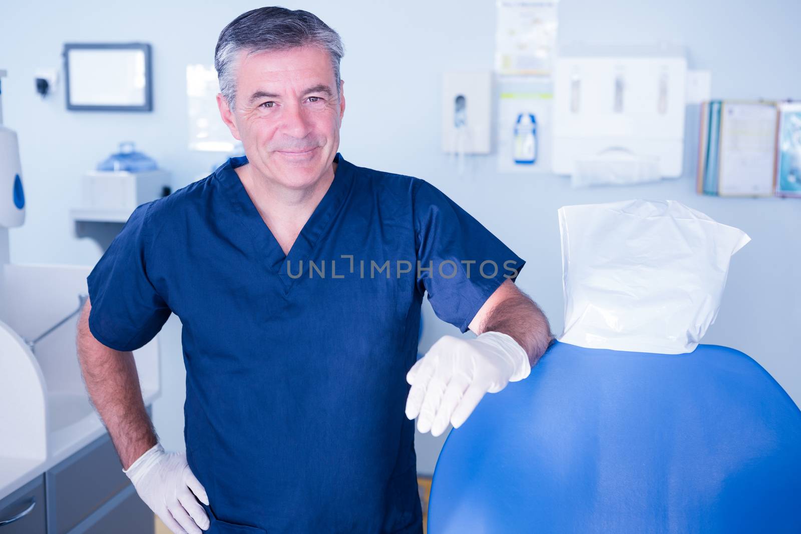 Dentist smiling at camera beside chair by Wavebreakmedia