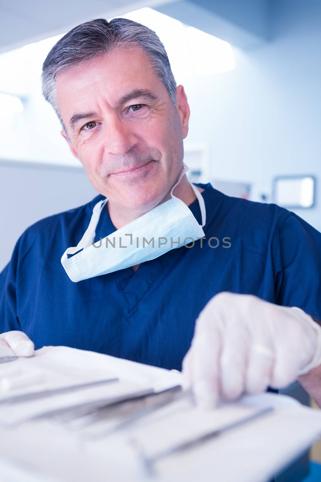 Dentist picking up tool and smiling at camera at the dental clinic