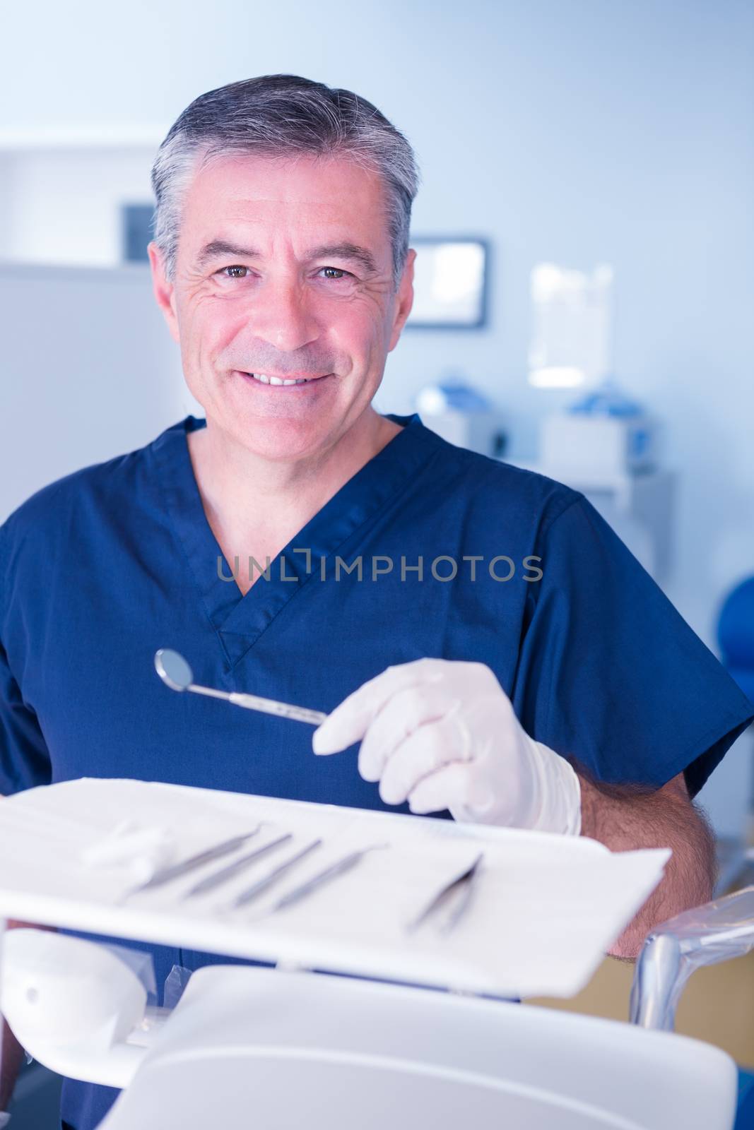 Dentist in blue scrubs smiling at camera holding tools by Wavebreakmedia