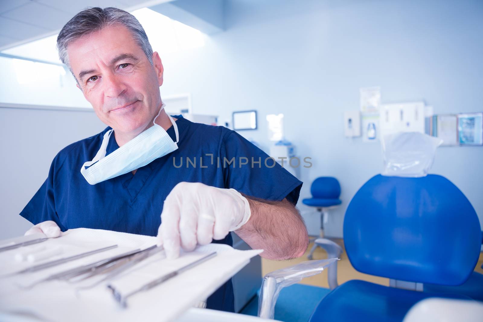 Dentist picking up tool and smiling at camera at the dental clinic