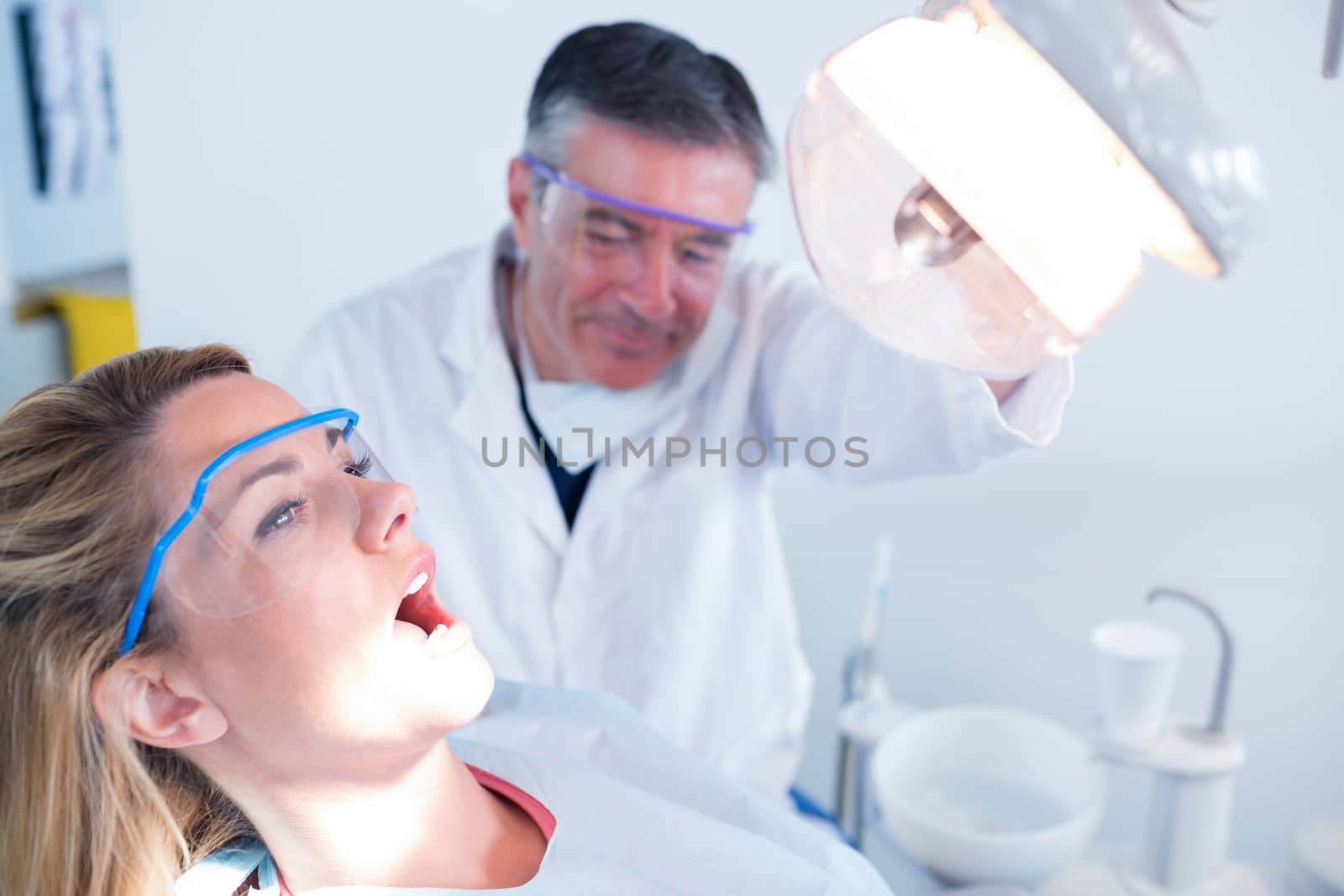 Dentist examining a patients teeth in chair under bright light by Wavebreakmedia