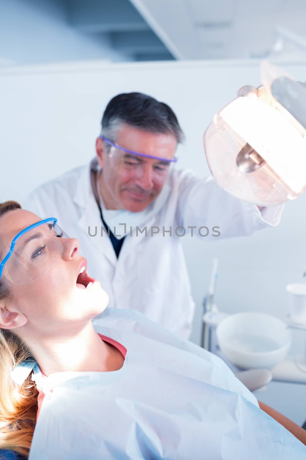 Dentist examining a patients teeth in chair under bright light at the dental clinic