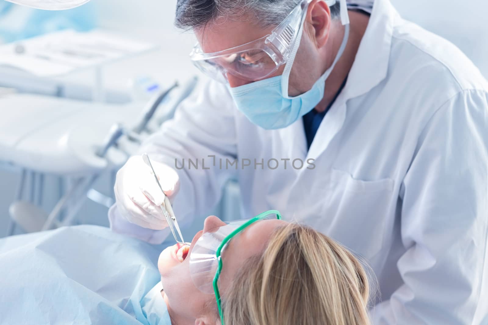 Dentist examining a patients teeth with surgical mask and gloves at the dental clinic