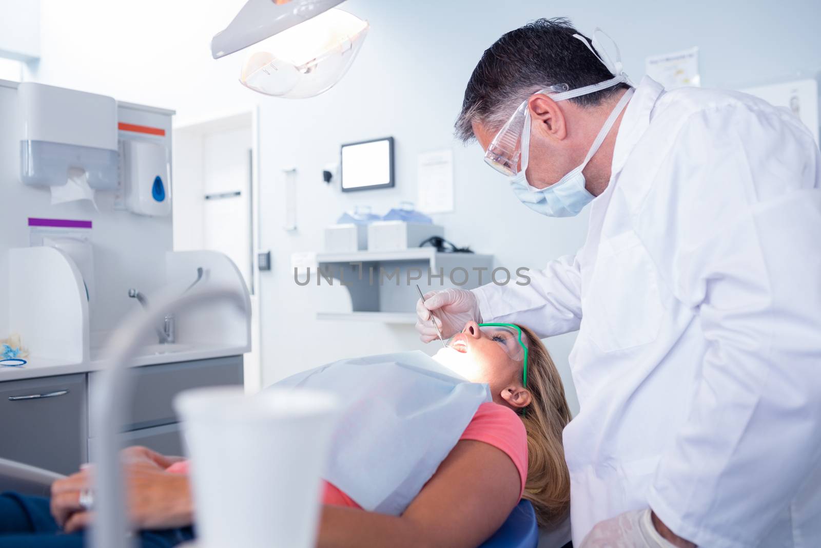 Dentist in surgical mask examining a patients teeth at the dental clinic