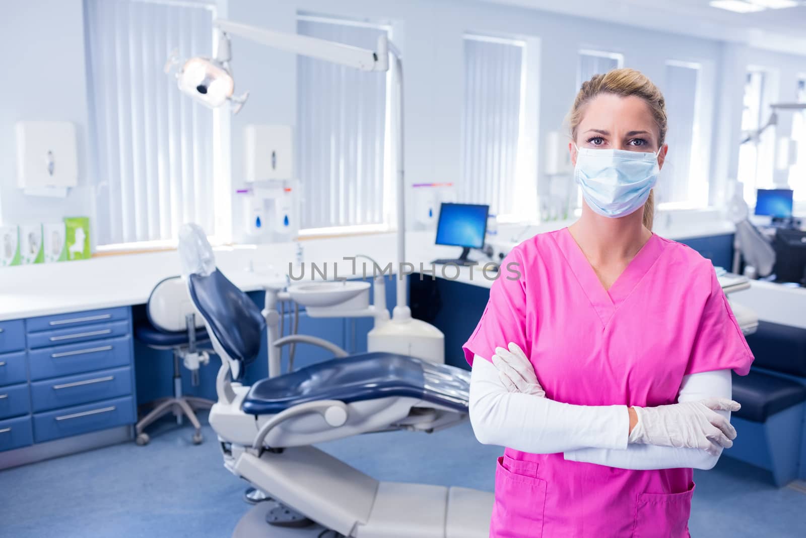Dentist in surgical mask standing with arms folded at the dental clinic