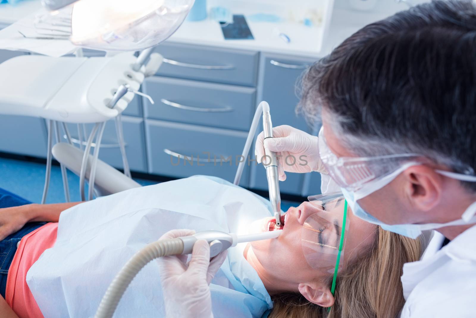 Dentist examining his patient with a suction hose at the dental clinic