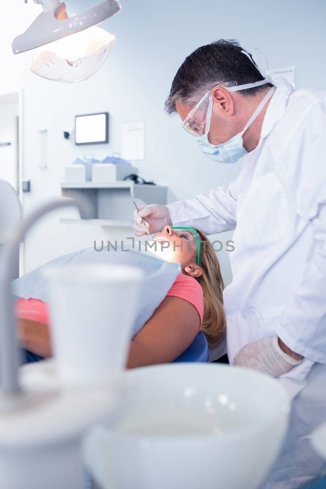 Dentist in surgical mask examining a patients teeth by Wavebreakmedia