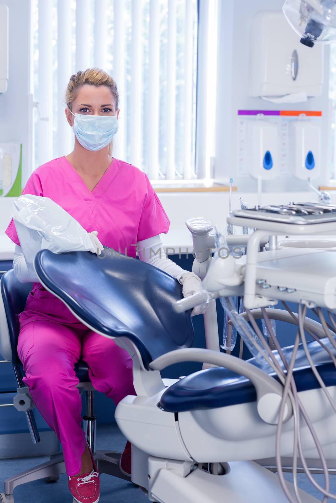 Dentist in pink scrubs looking at camera beside chair by Wavebreakmedia