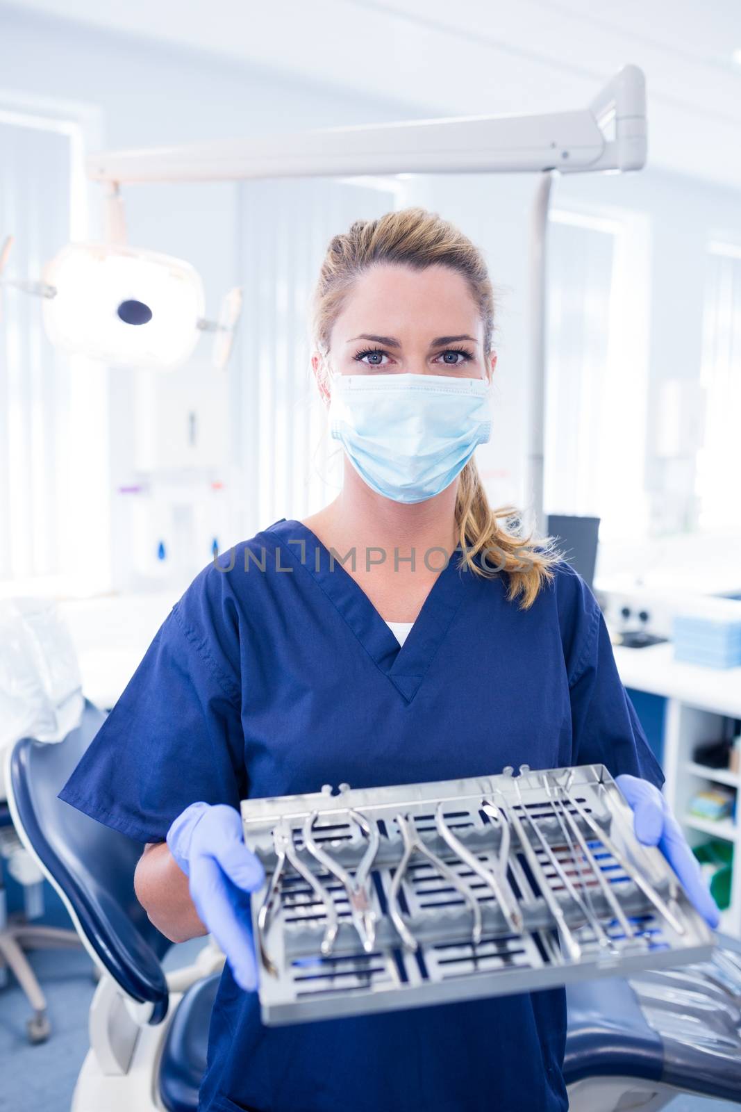 Dentist in blue scrubs offering tray of tools by Wavebreakmedia