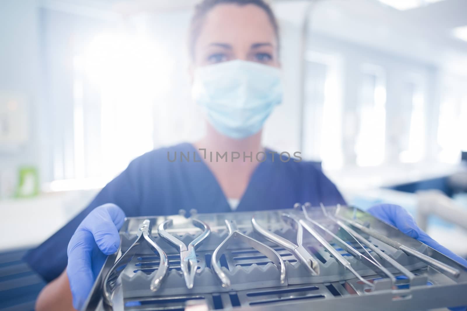 Dentist in blue scrubs showing tray of tools at the dental clinic