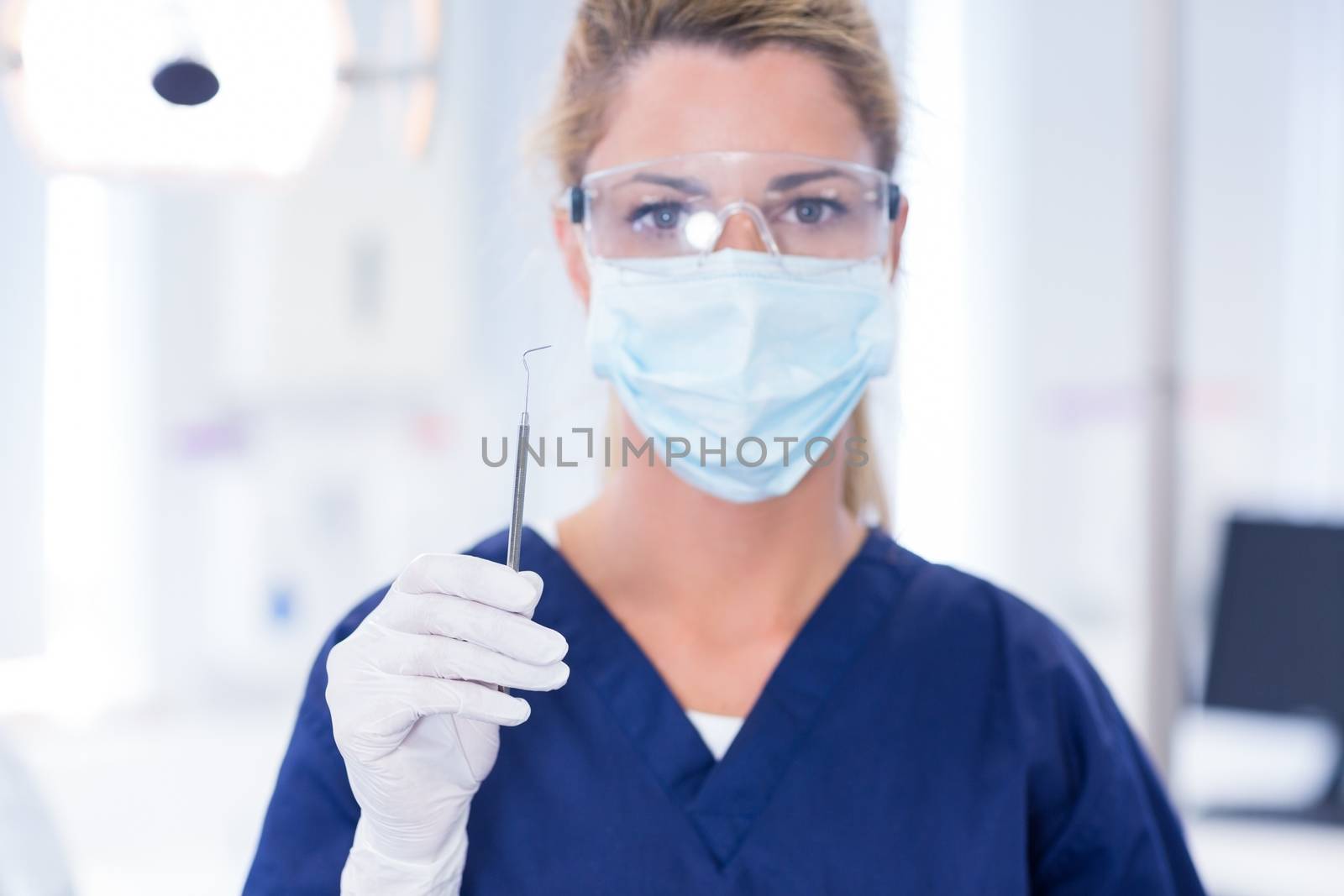 Dentist in mask holding dental explorer at the dental clinic