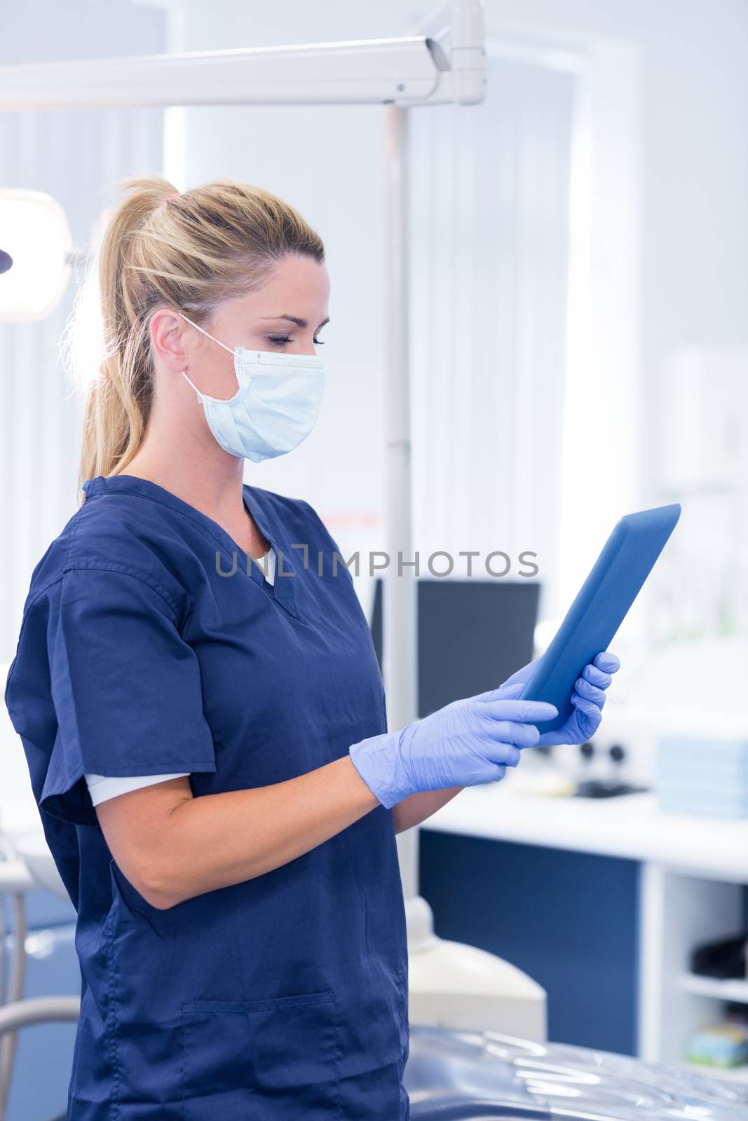 Dentist in mask and blue scrubs using her tablet by Wavebreakmedia
