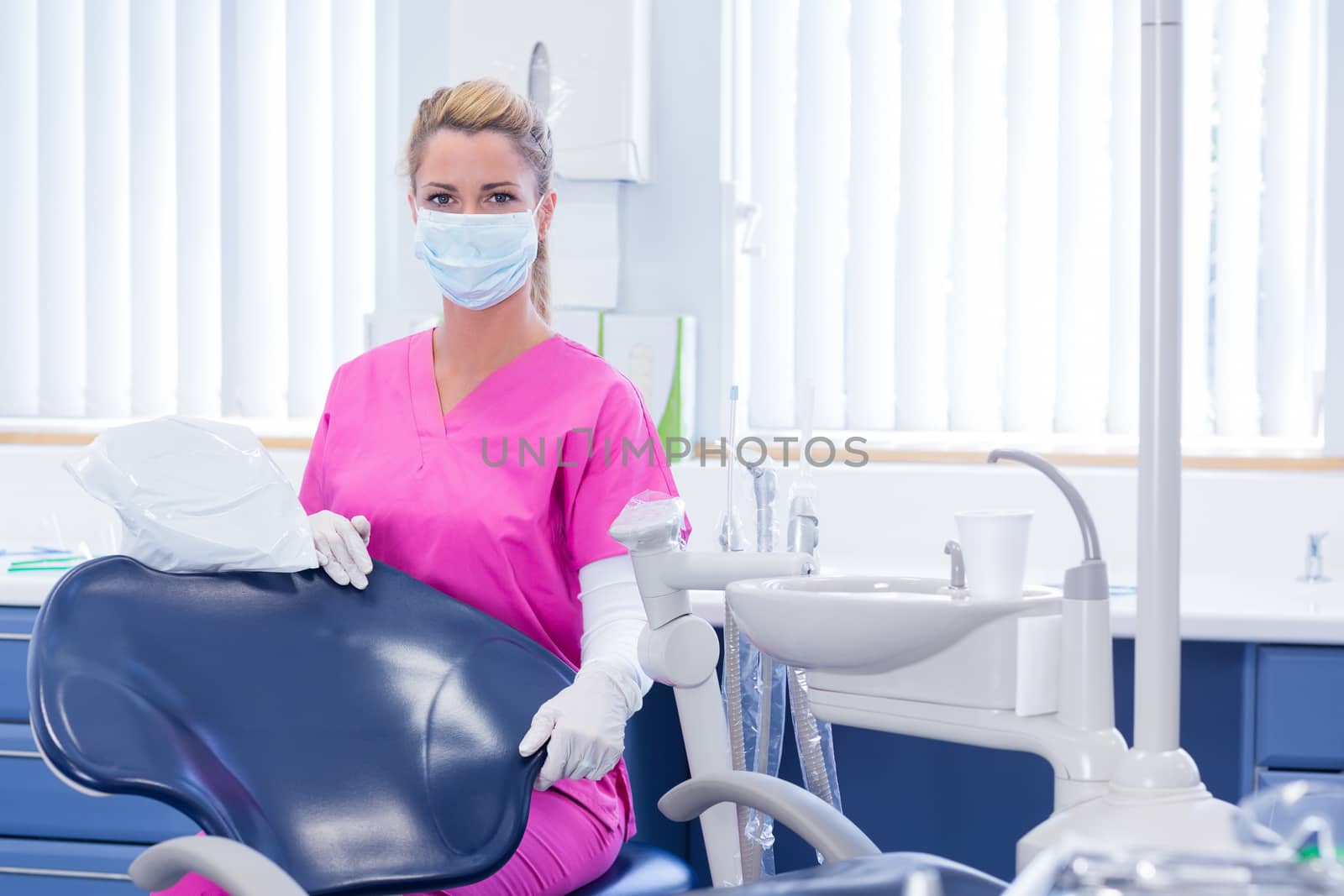 Dentist in mask looking at camera beside chair at the dental clinic