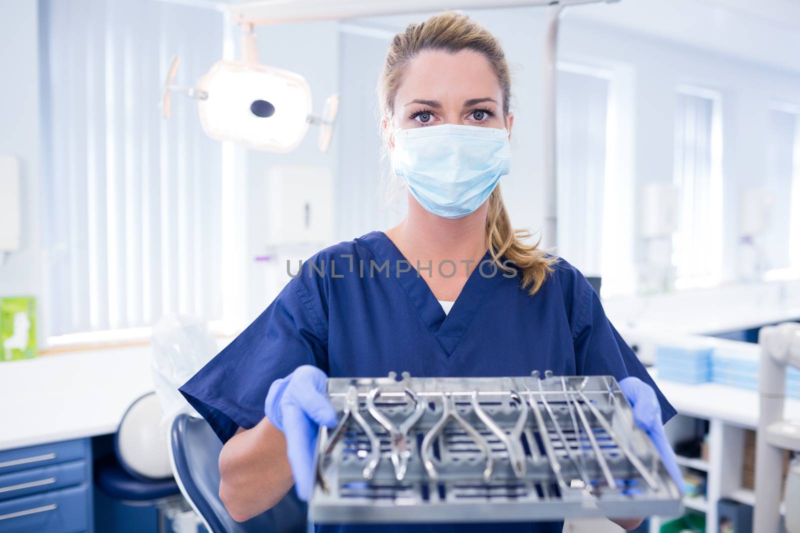 Dentist in blue scrubs holding tray of tools at the dental clinic