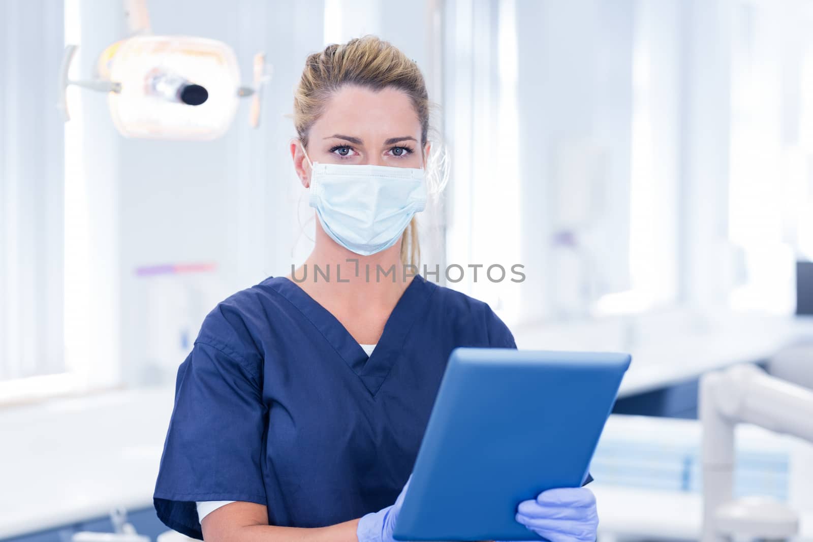 Dentist in mask using her tablet and looking at camera at the dental clinic