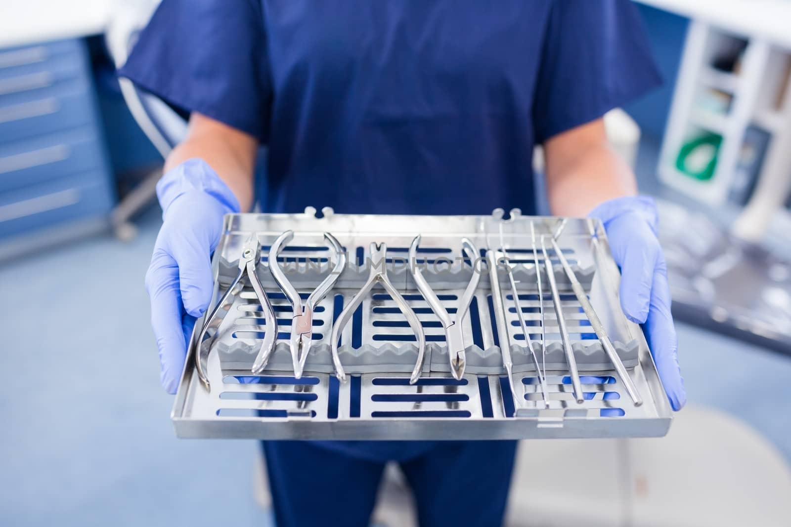 Dentist in blue scrubs holding tray of tools at the dental clinic