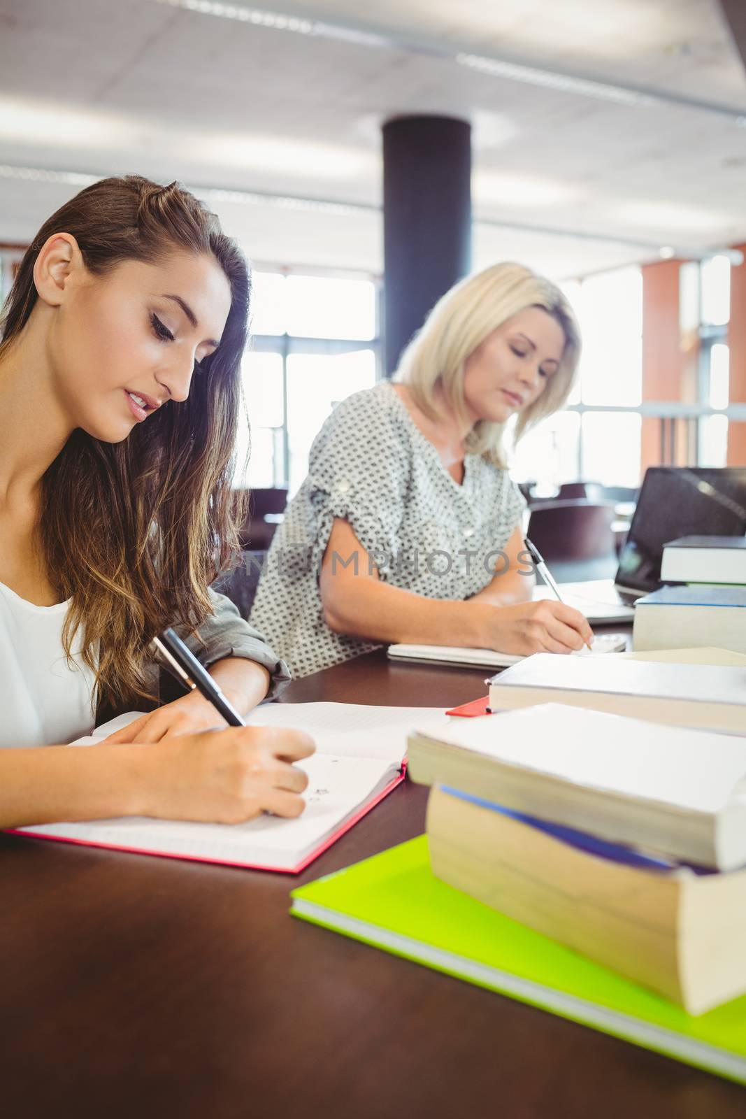 Matures females students writing notes at desk in library