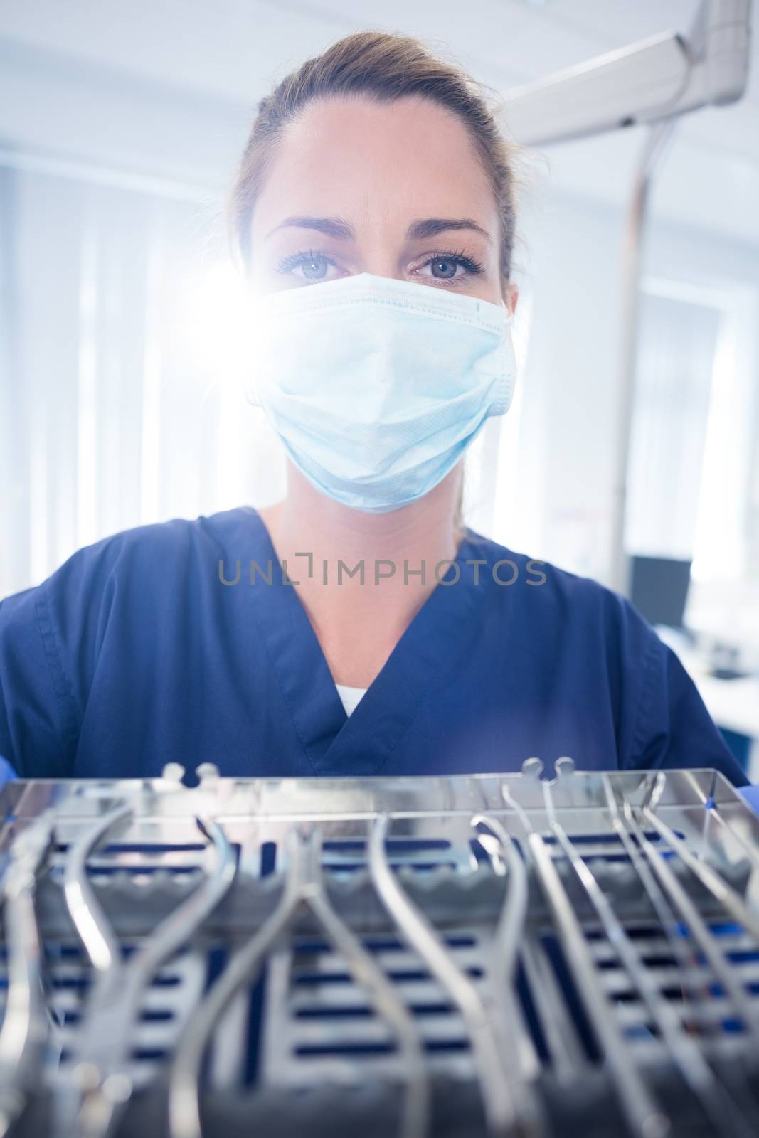 Dentist in blue scrubs showing tray of tools by Wavebreakmedia