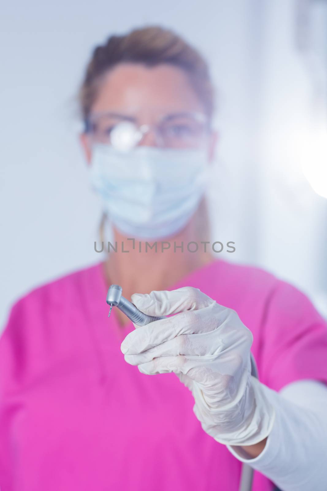 Dentist in surgical mask and scrubs holding tool at the dental clinic