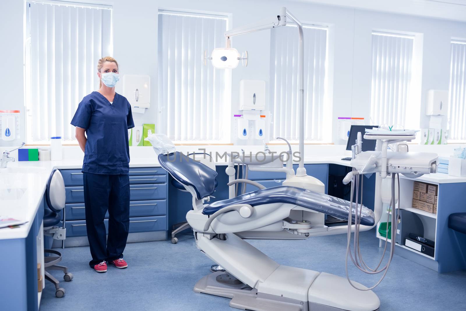 Dentist in blue scrubs standing beside chair at the dental clinic