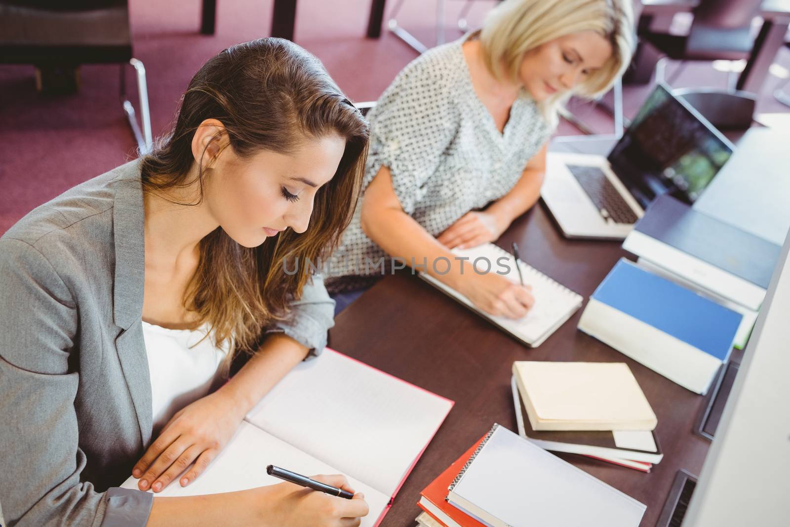 Matures females students writing notes at desk in library