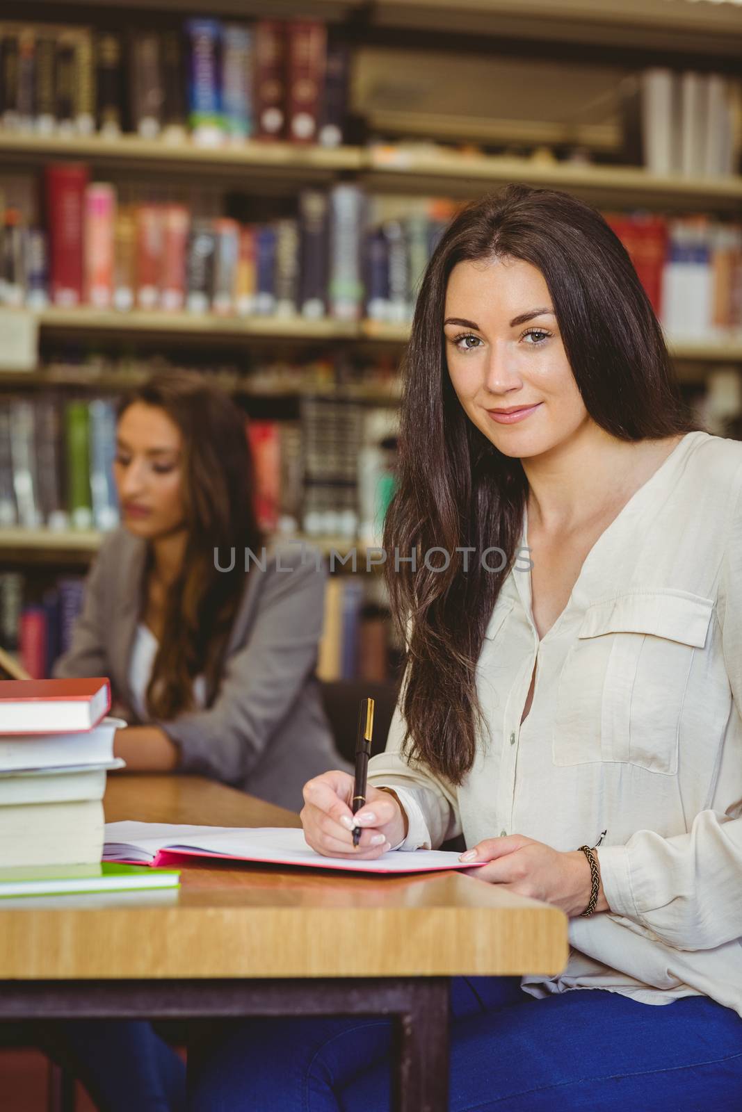 Happy student sitting at desk writing smiling at camera in library