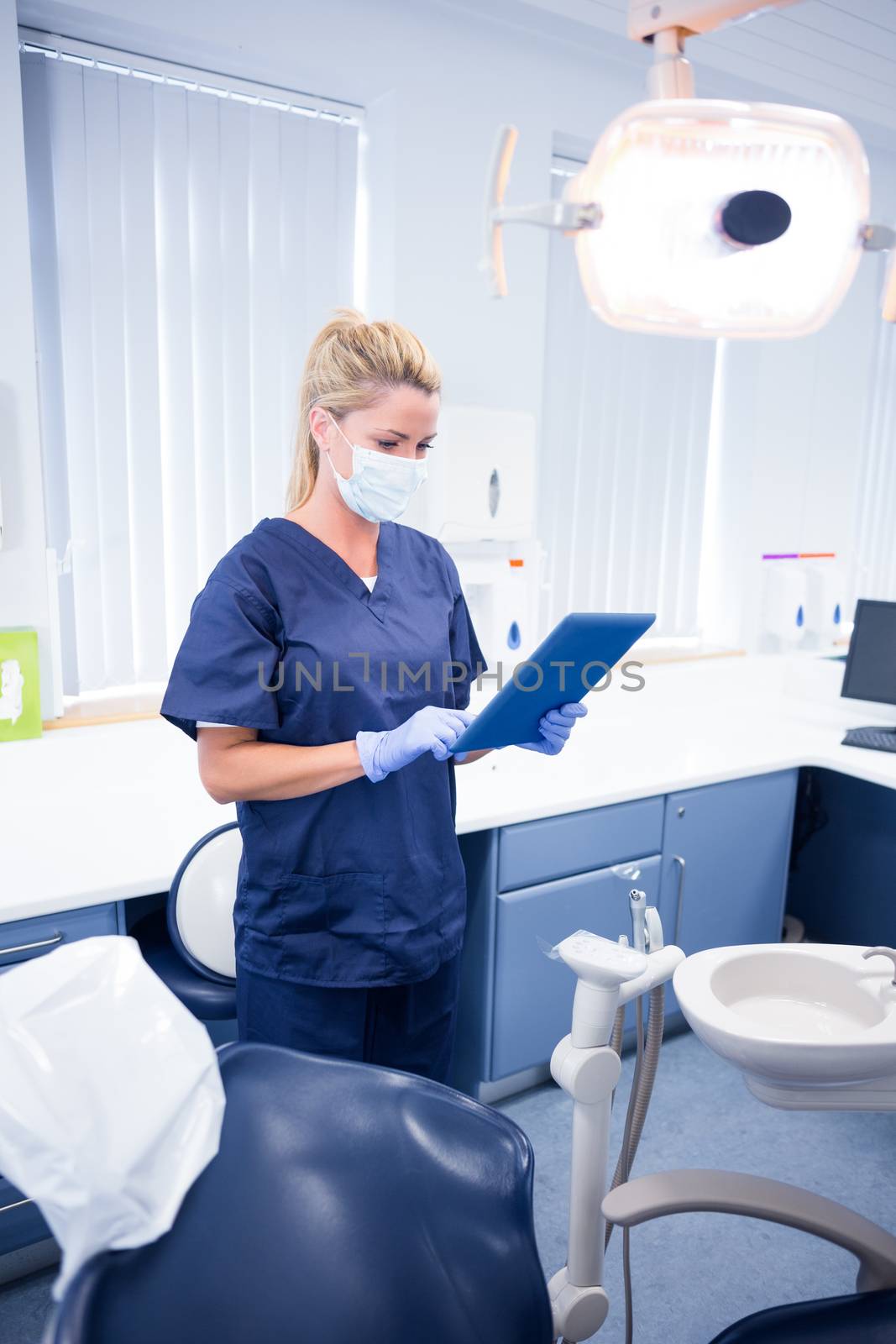 Dentist in mask and blue scrubs using her tablet at the dental clinic