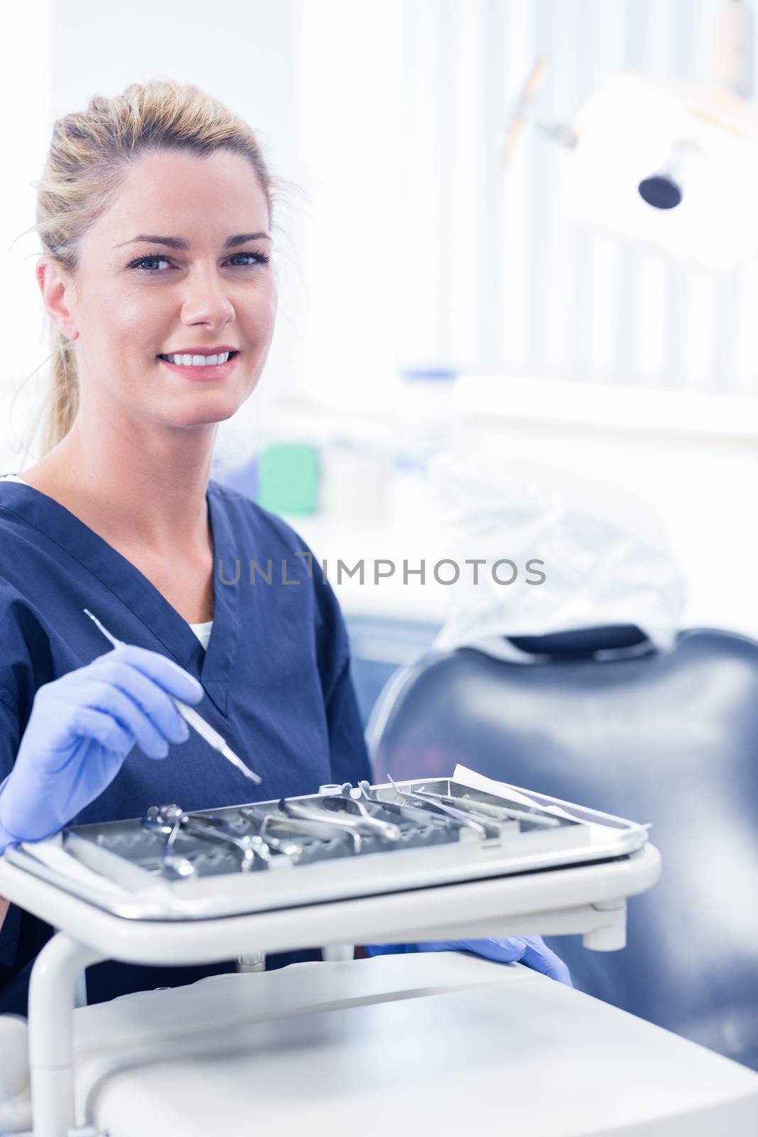 Dentist sitting with tray of tools smiling at camera by Wavebreakmedia
