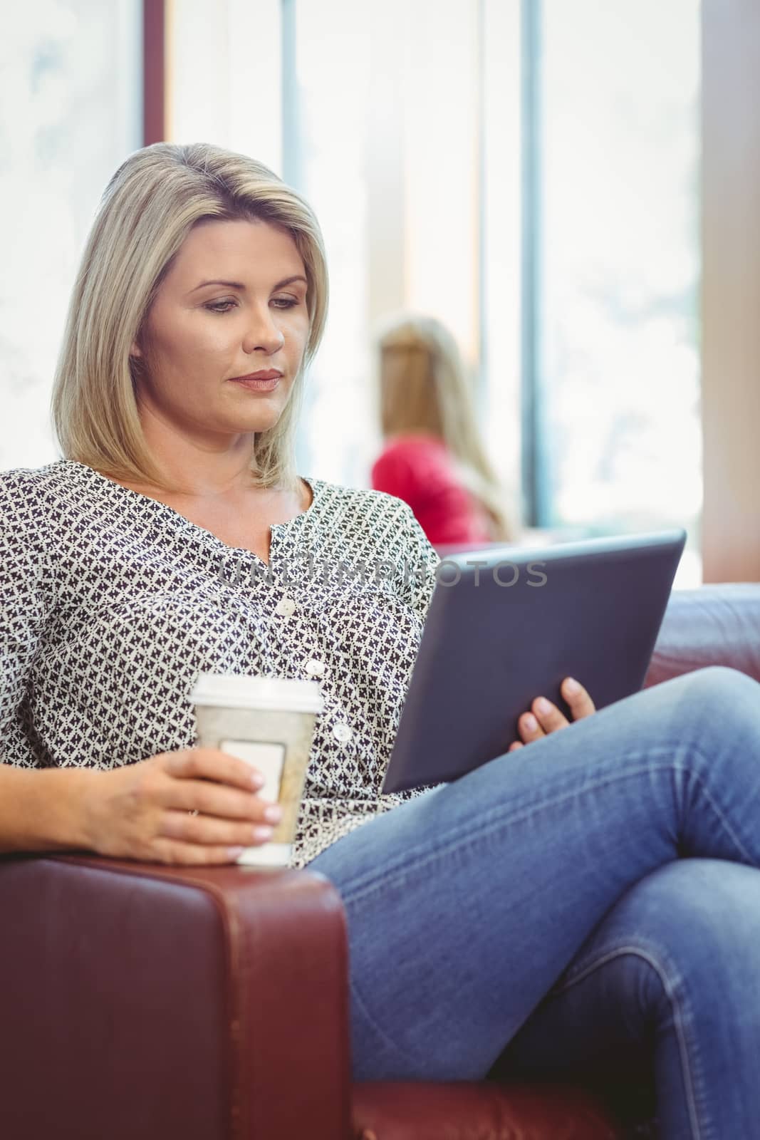 Woman using digital tablet and holding disposable cup in library