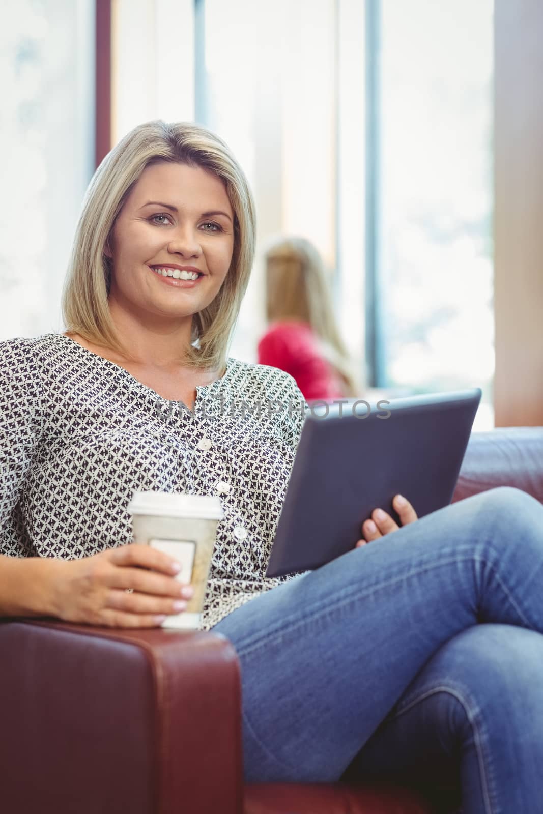 Smiling girl using digital tablet and holding disposable cup in library