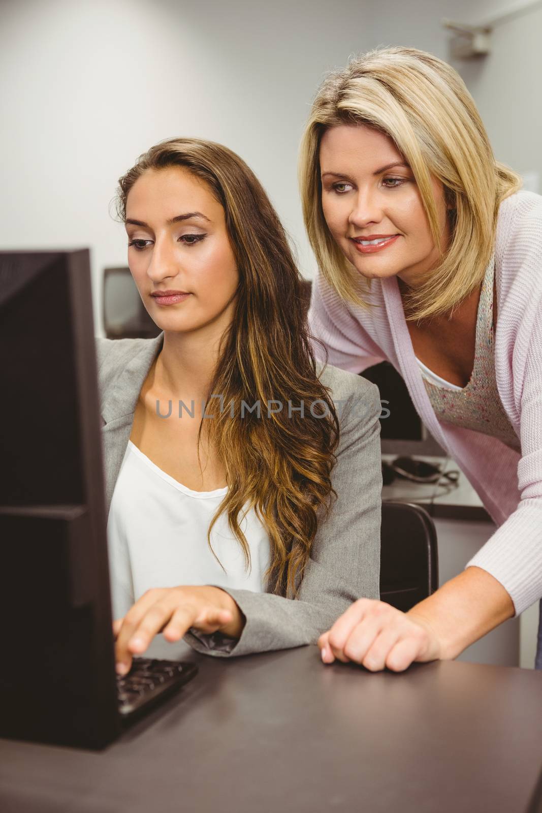 Smiling teacher and student behind desk at computer in computer room 