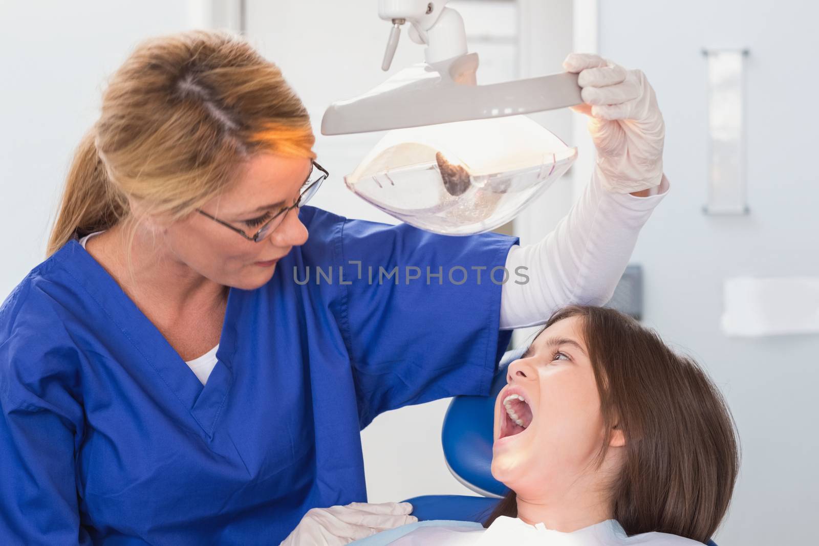 Pediatric dentist examining with a light her young patient in dental clinic
