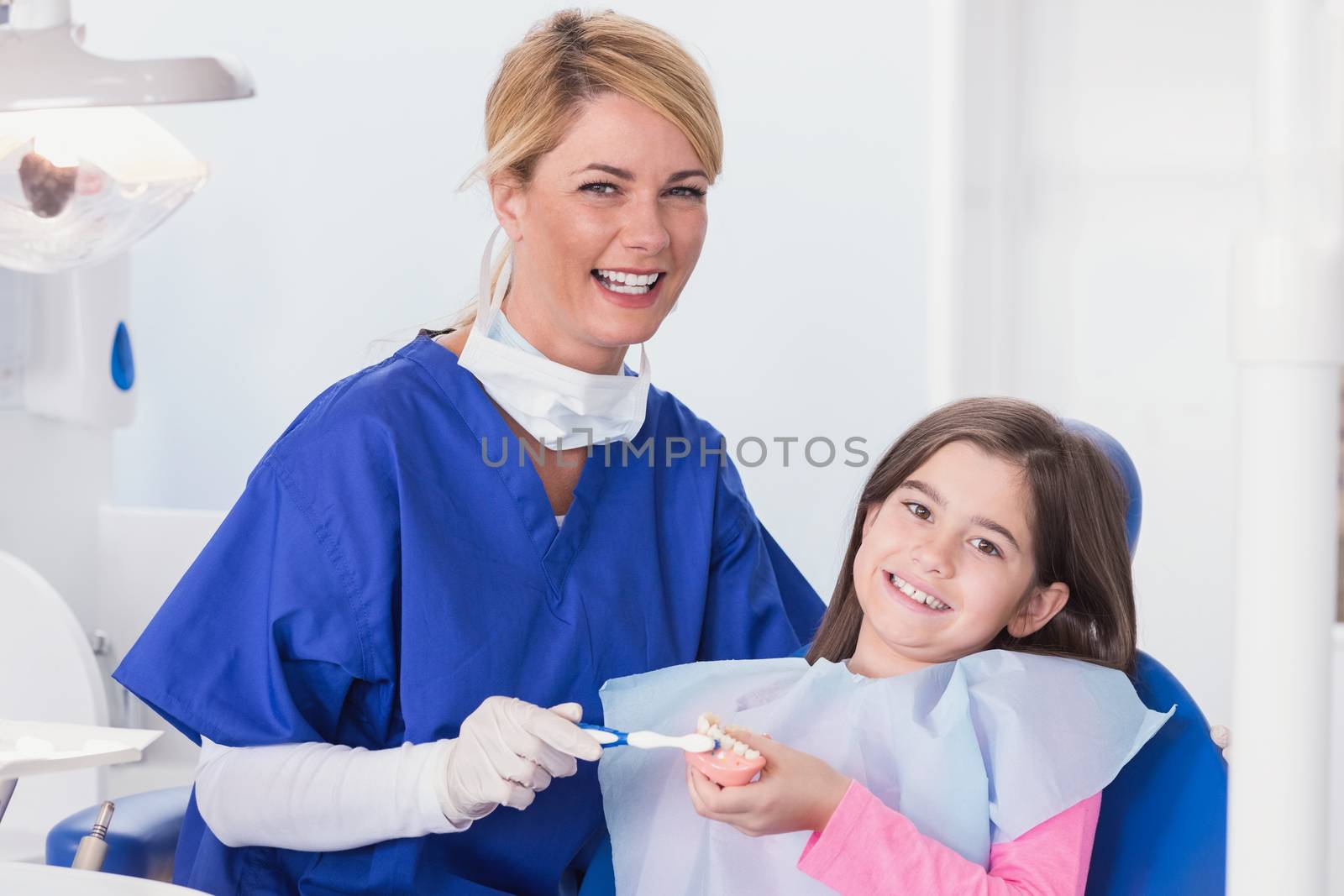 Smiling dentist teaching to her young patient how use toothbrush in dental clinic