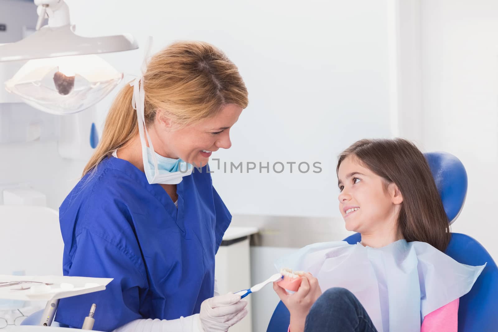 Smiling dentist teaching to her young patient how use toothbrush in dental clinic