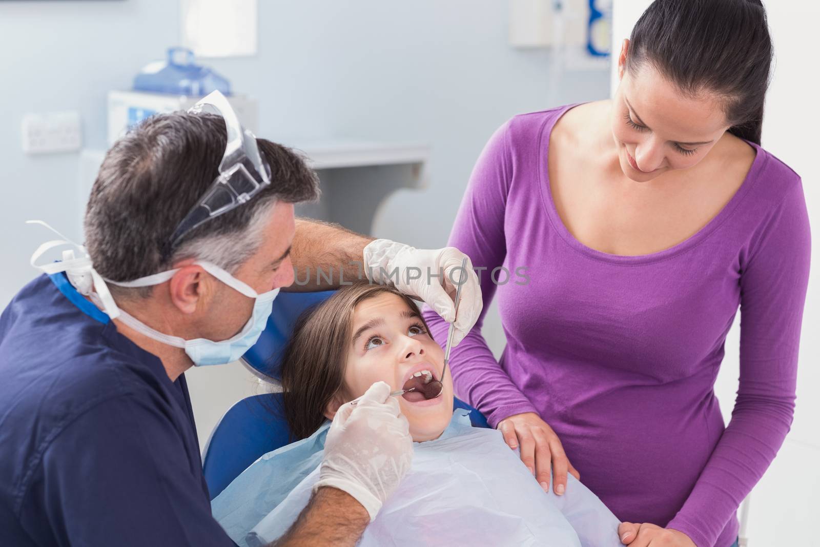 Pediatric dentist examining young patient with her mother in dental clinic