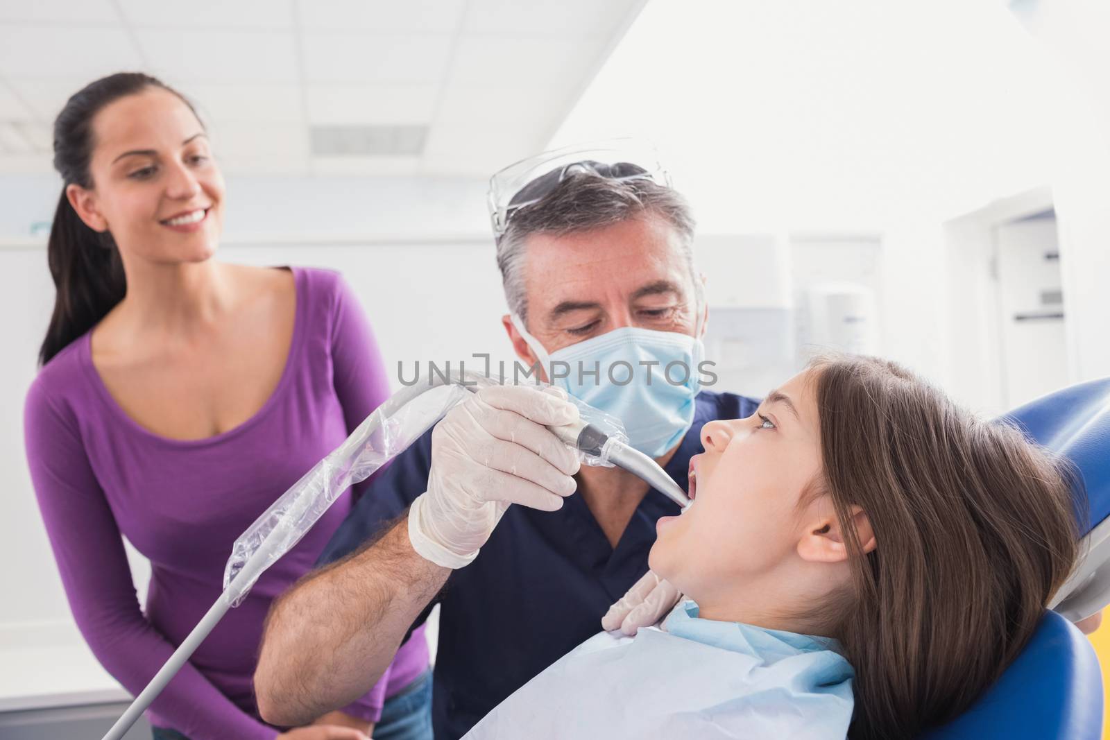 Pediatric dentist examining young patient with a suction tube by Wavebreakmedia